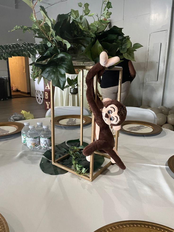 there is a stuffed monkey hanging from the top of a table with greenery on it