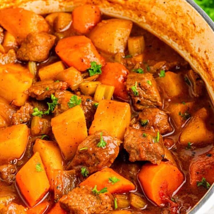 a pot filled with meat and vegetables on top of a blue towel next to some parsley