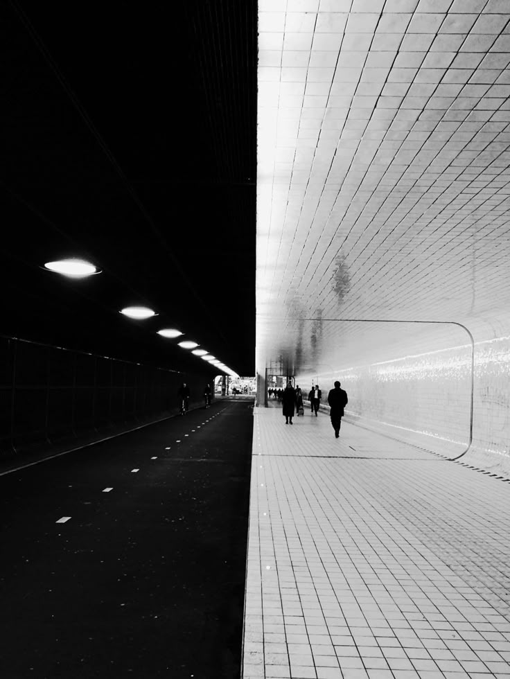 black and white photograph of people walking in a subway station at night time with lights on