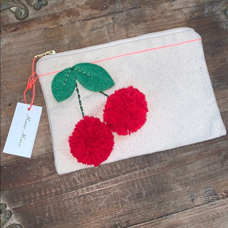 two cherries with green leaves and red pom - poms on a white pouch