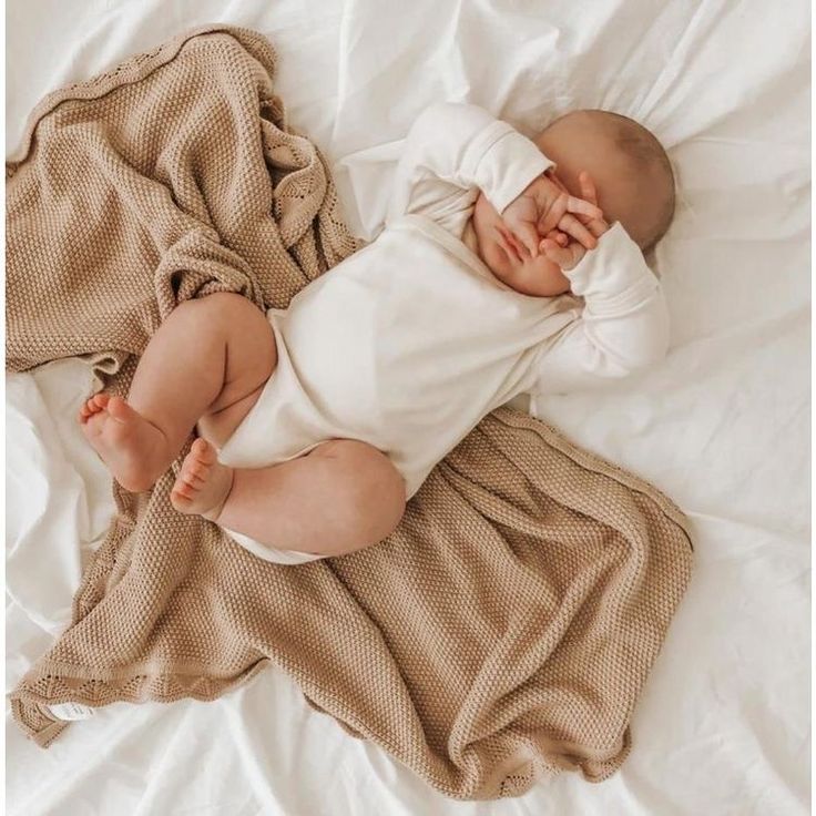 a baby laying on top of a white bed next to a brown and tan blanket