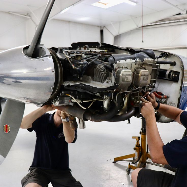 two men working on an airplane in a hanger with the propeller still attached to it