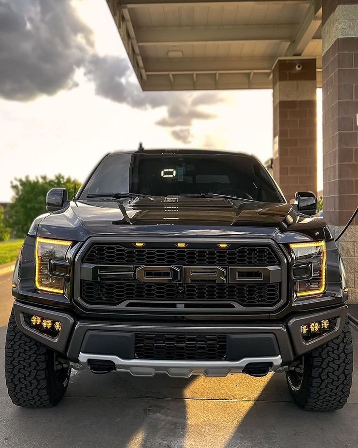 the front end of a black truck parked in a parking lot next to a building