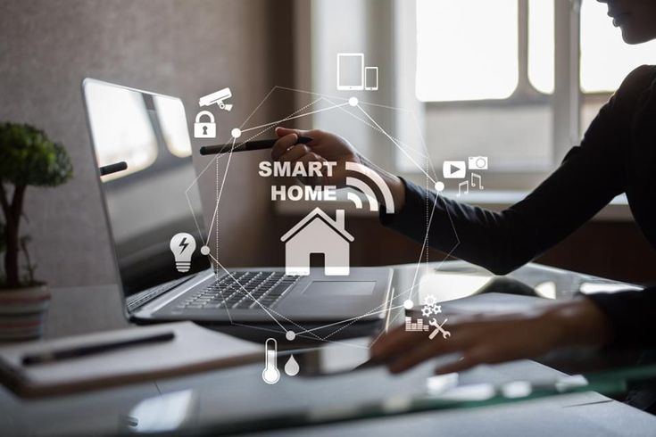 a woman sitting at a desk working on a laptop with smart home icons coming out of the screen