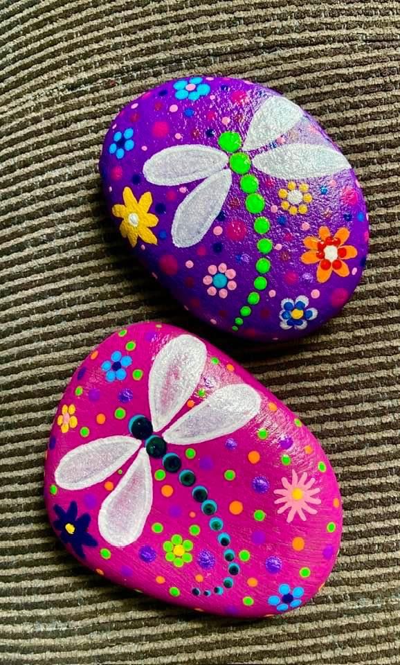 two painted rocks with flowers and dragonflies on them