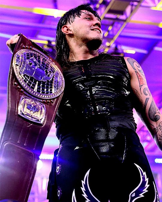 a man holding a wrestling belt in his right hand and looking up at the sky