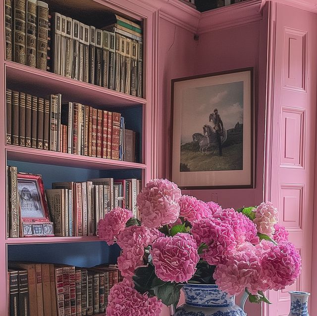 pink flowers are in a blue and white vase on a table next to bookshelves