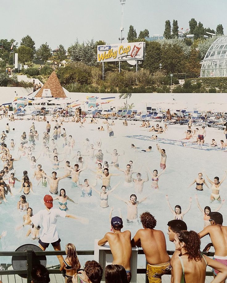 a large group of people are in the water at an outdoor swimming pool and some have no shirts on