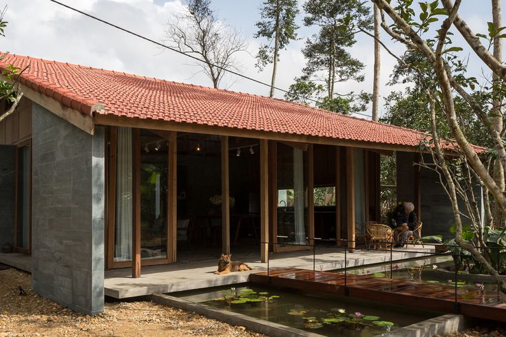 the house is made out of concrete and has a red tiled roof, surrounded by trees