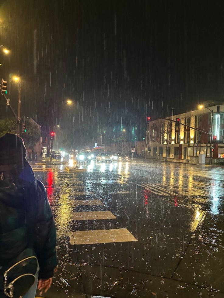 a person standing in the rain on a city street with an umbrella over their head