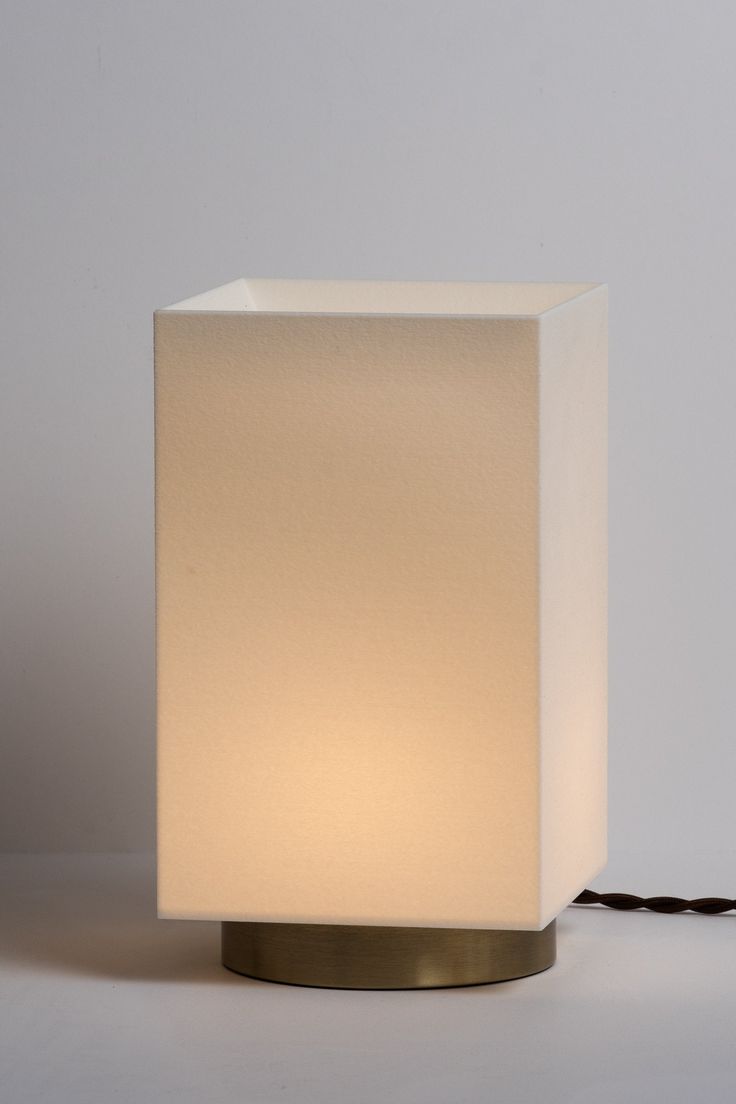 a white square lamp sitting on top of a table next to a black cord that is plugged in