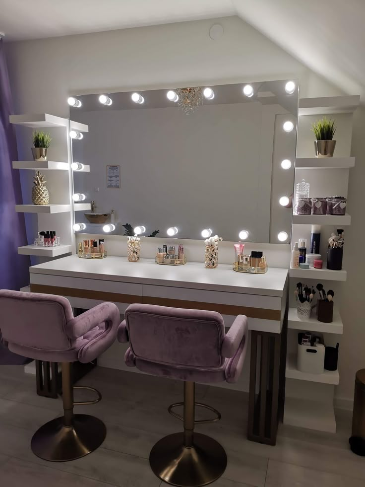 two purple chairs sitting in front of a mirror with lights on it's sides