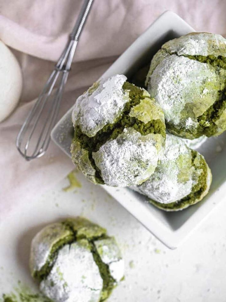 powdered sugar covered pastries in a white dish next to an egg whisk