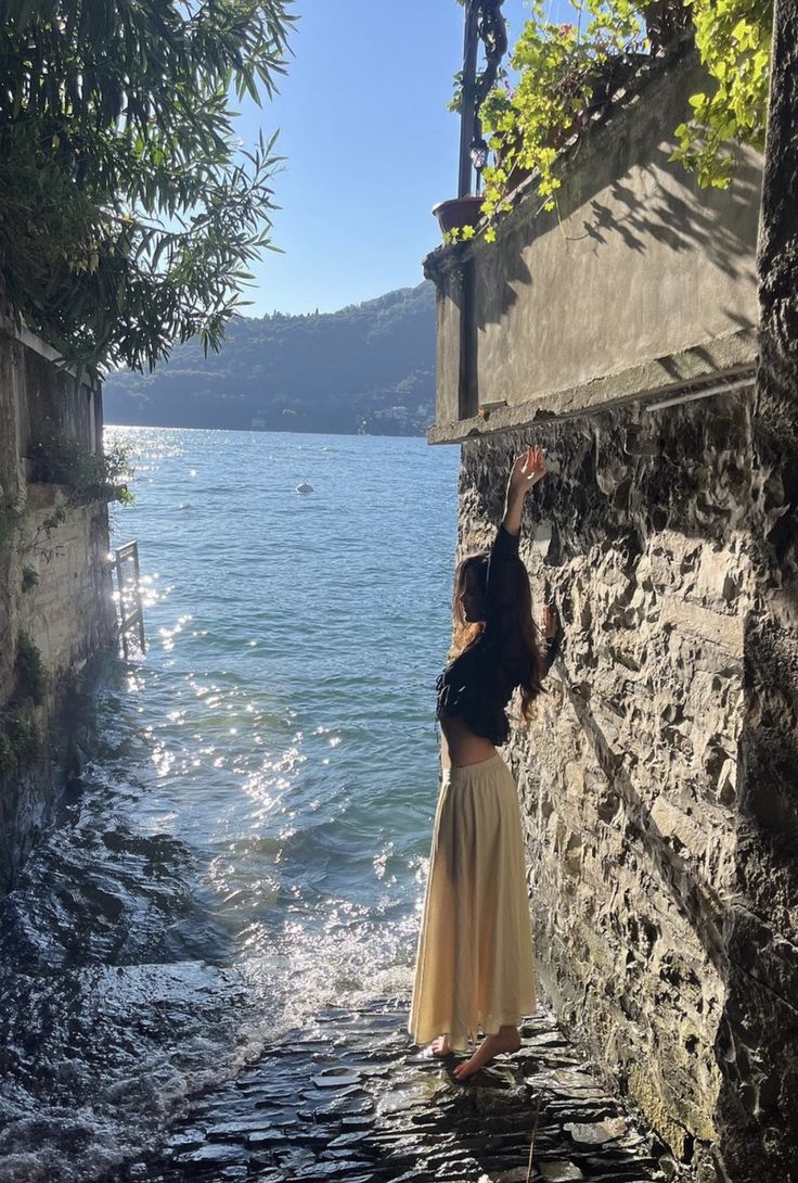 a woman standing on the edge of a stone wall next to a body of water