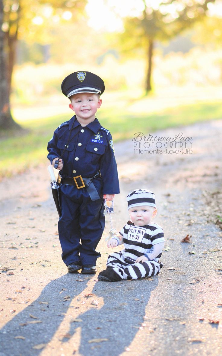 two young boys dressed in police uniforms standing next to each other on a dirt road