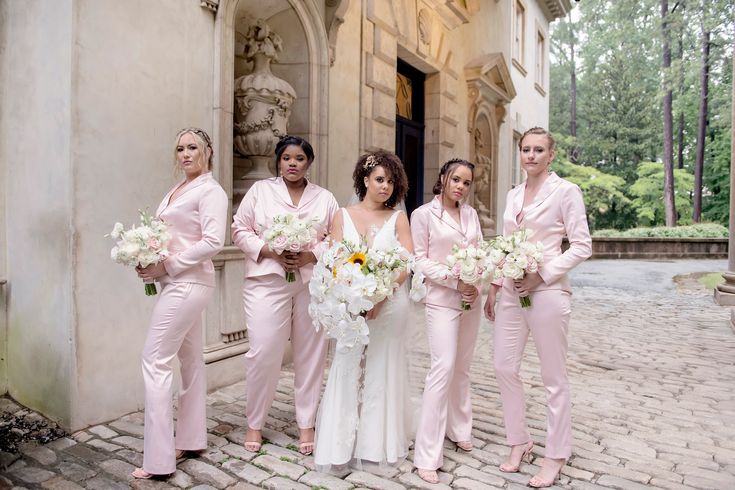 a group of women standing next to each other in front of a building holding bouquets