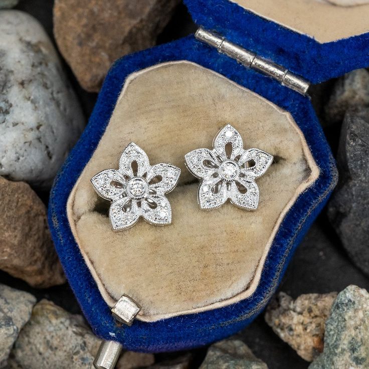 These elegant diamond flower earrings feature and open flower design with a round brilliant cut diamond set into a bezel in the center. Each petal is set with three (3) round brilliant diamond accents and finished with milgrain edging. The earrings are crafted in 14k white gold. We have a few pairs of these. Elegant Flower Shaped Diamond Earrings With Prong Setting, Diamond Flower Earrings With Prong Setting For Wedding, Formal Diamond Earrings With Flower Shape, Formal Flower Shaped Diamond Earrings With Accents, Diamond Flower Shaped Earrings For Formal Events, Diamond Flower Shaped Earrings For Formal Occasions, Formal White Gold Flower Earrings With Diamond Accents, Classic Flower Earrings With Diamond Accents, Elegant Brilliant Cut Diamond Earrings In Flower Shape