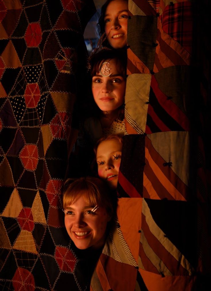 four girls peeking out from behind a quilt