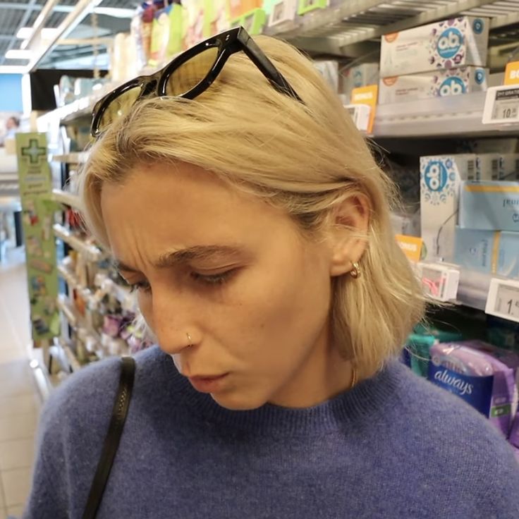 a blonde woman wearing glasses looking at her cell phone in a store aisle with other items on the shelves behind her