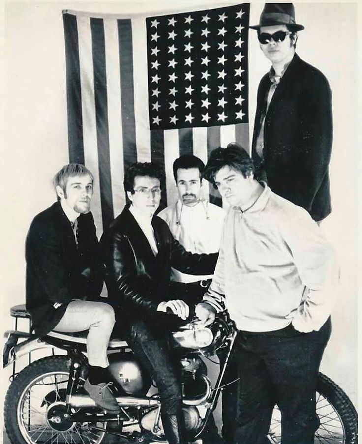 black and white photograph of men on motorcycle in front of an american flag