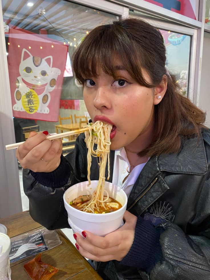 a woman eating noodles with chopsticks at a restaurant