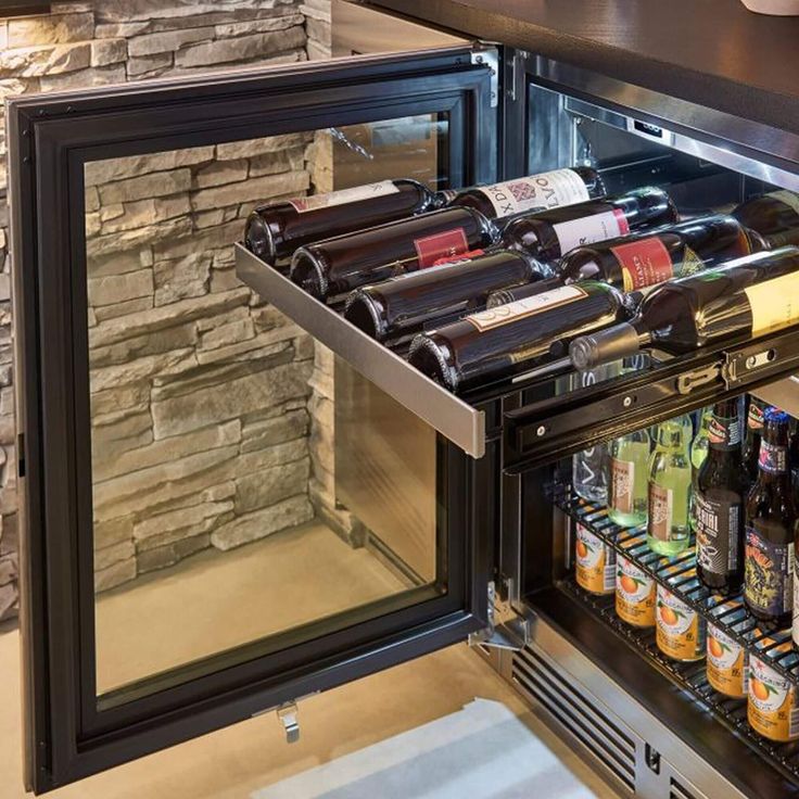 an open refrigerator filled with bottles of wine and beer next to a stone wall behind it