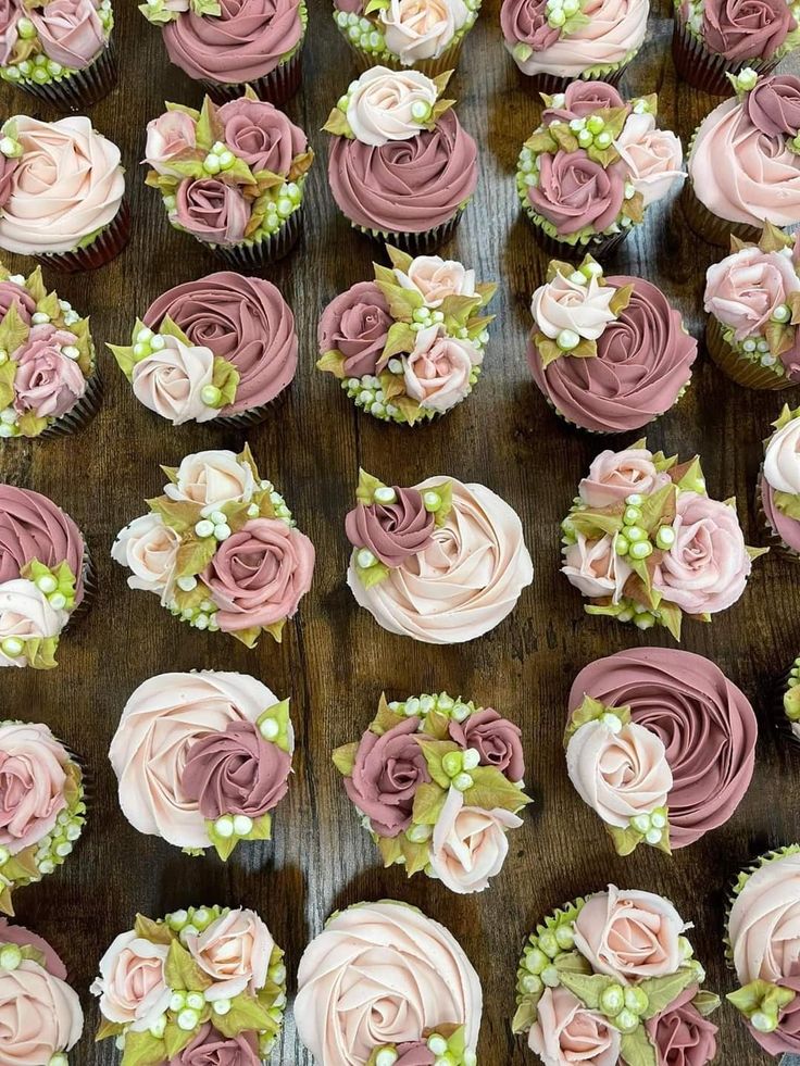 cupcakes with pink and white frosting flowers on wooden table next to each other