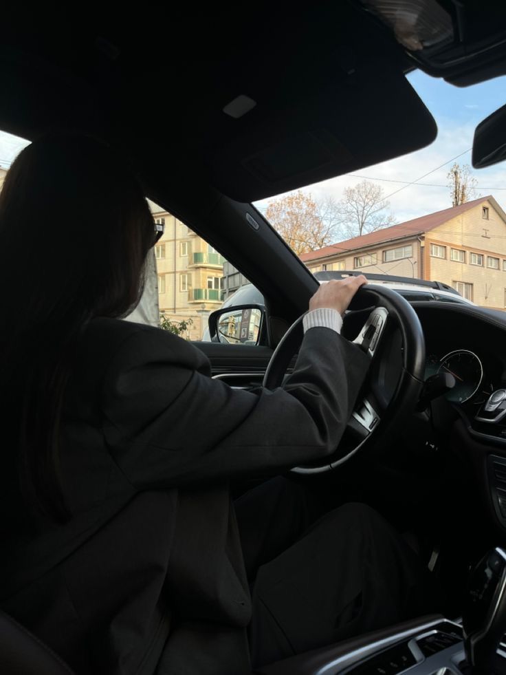 a woman driving a car on a city street with buildings in the backgroud