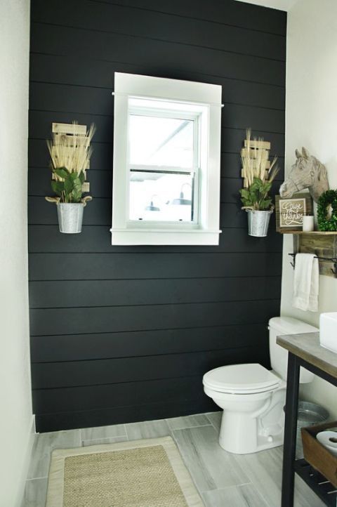 a white toilet sitting next to a bathroom sink under a window in a black wall