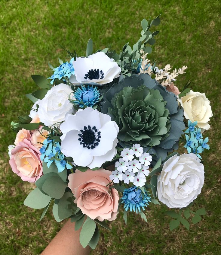 a person holding a bouquet of flowers in their hand on the grass with other flowers