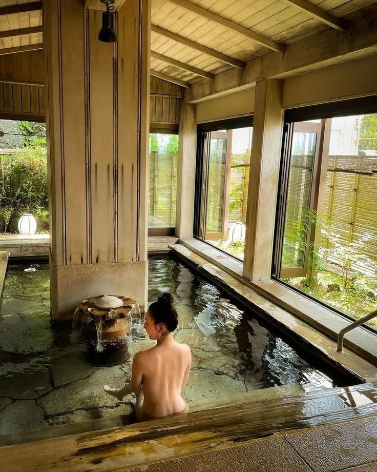 a person sitting in a hot tub inside of a building with large windows on the side