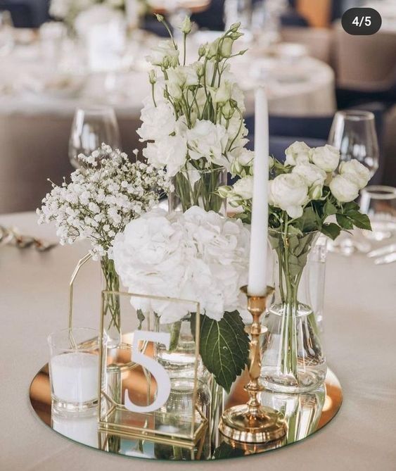 white flowers in vases and candles are on a table with silverware, glasses and napkins