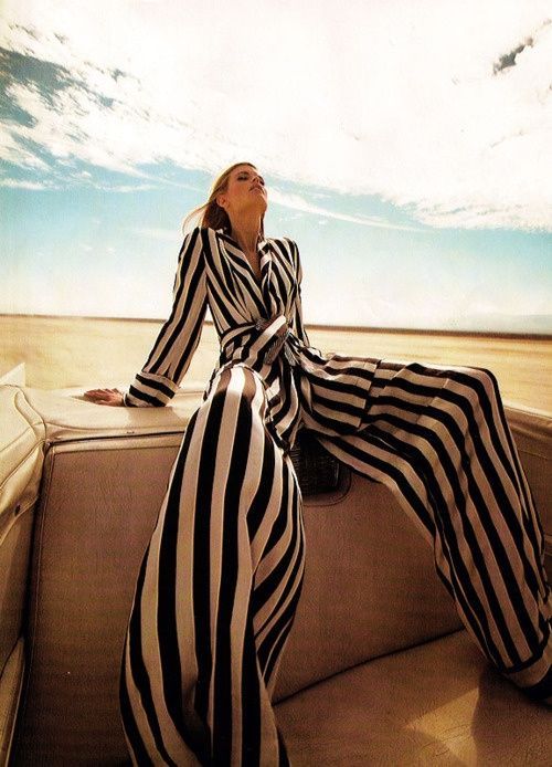 a woman sitting on the back of a boat in striped dress and heels with her legs crossed