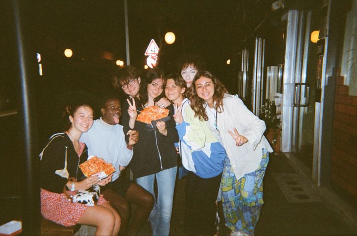 a group of young people standing next to each other in front of a building at night