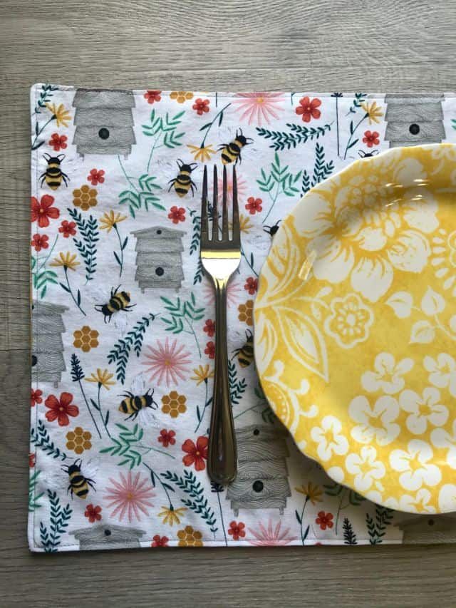 a yellow and white placemat with flowers on it, next to a fork and knife