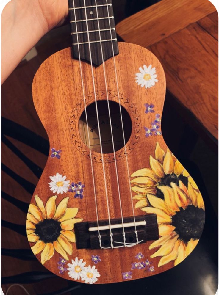 a wooden ukulele with sunflowers painted on it's body and strings