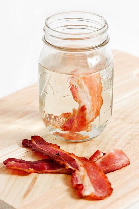 a glass jar filled with bacon sitting on top of a wooden cutting board