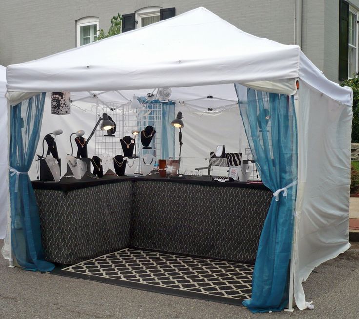 a white tent with blue drapes on the sides and black chairs under it in front of a building