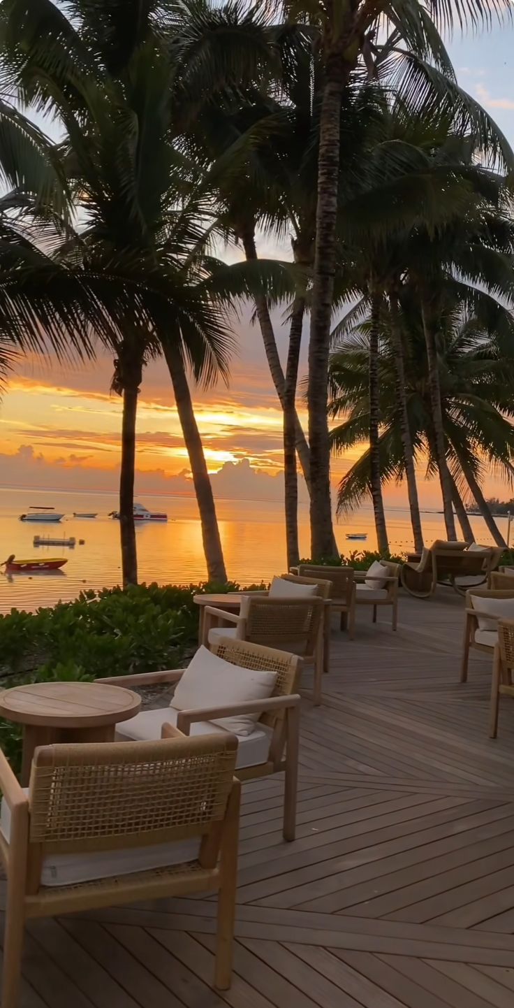 the sun is setting over the ocean with palm trees and lounge chairs on the deck