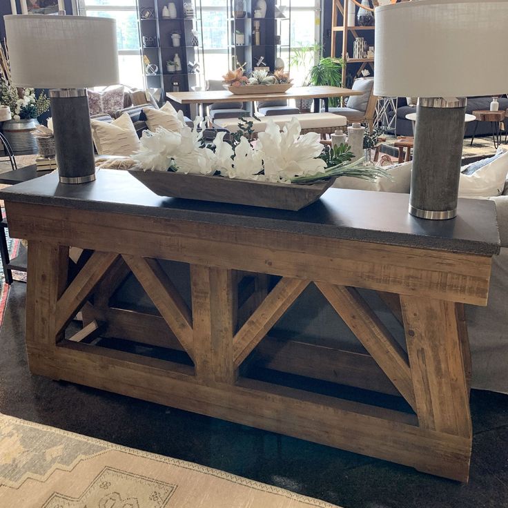 a wooden table with two lamps on top and flowers in a bowl sitting on it