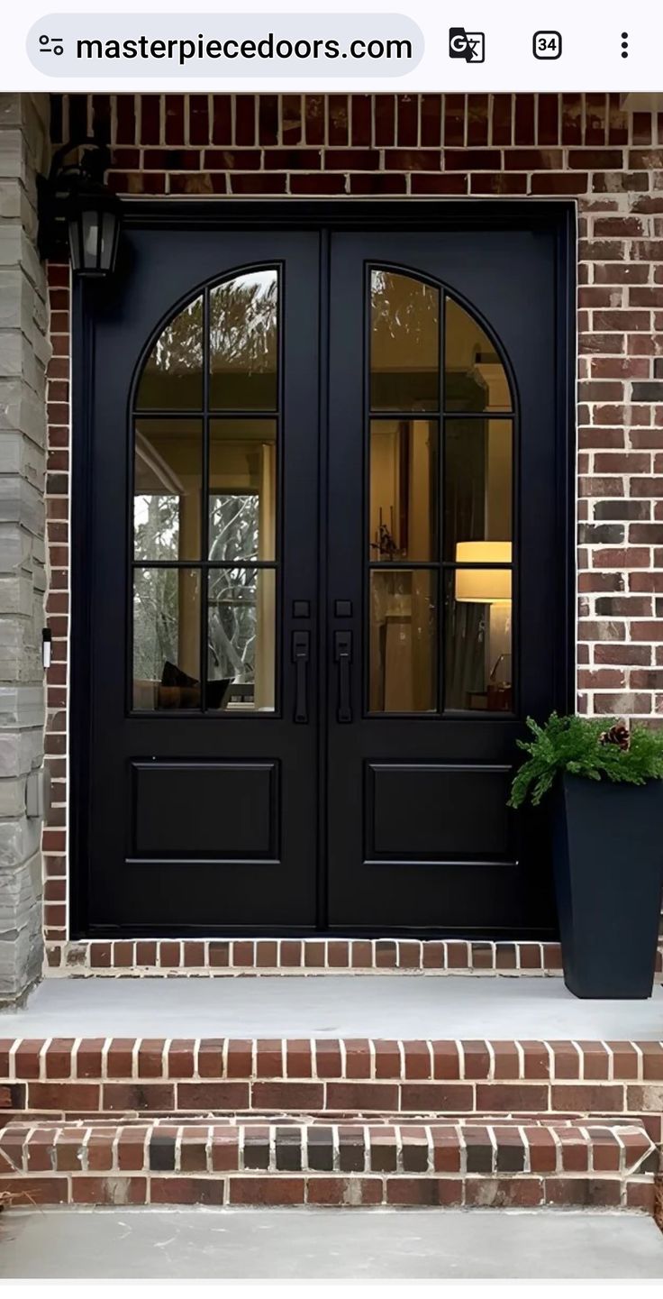 a black front door with two potted plants on the steps and brick wall behind it