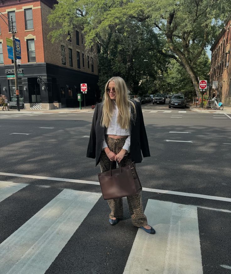 a woman standing in the middle of a crosswalk holding a brown bag and wearing sunglasses