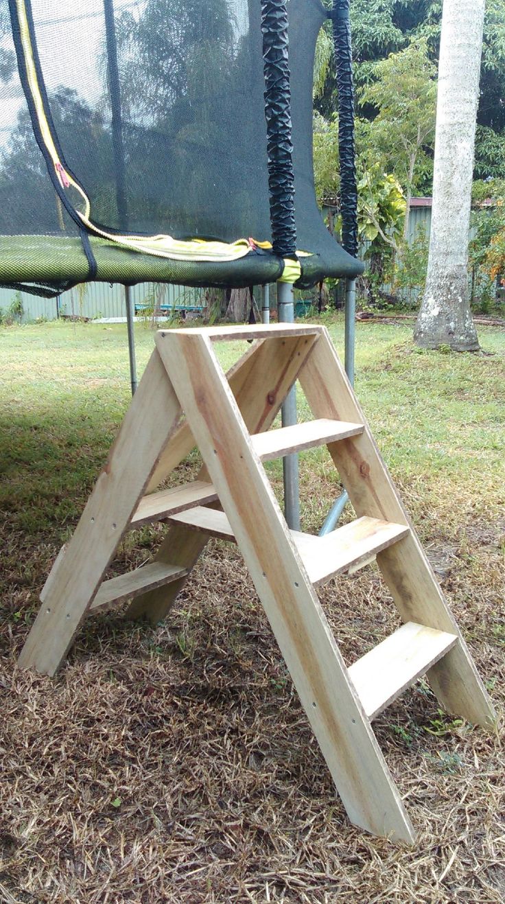 there is a ladder made out of wood in the grass next to a trampoline