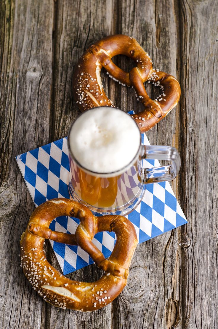 two pretzels and a mug of beer on a wooden table with checkered napkins