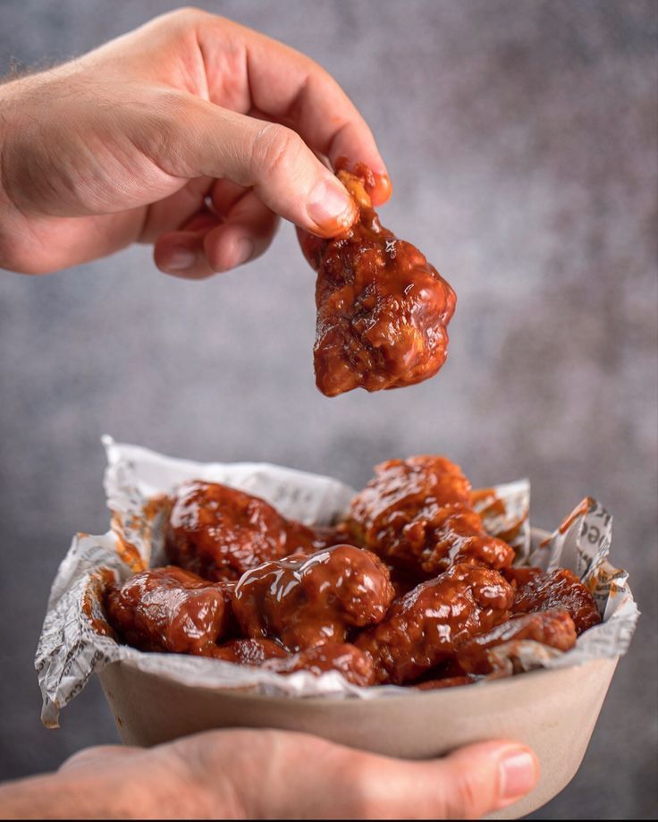 someone is holding up some meatballs in a paper bowl and dipping them into sauce