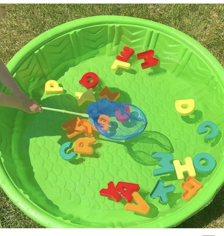 a child's hands playing with letters and numbers in a green plastic bowl on the grass