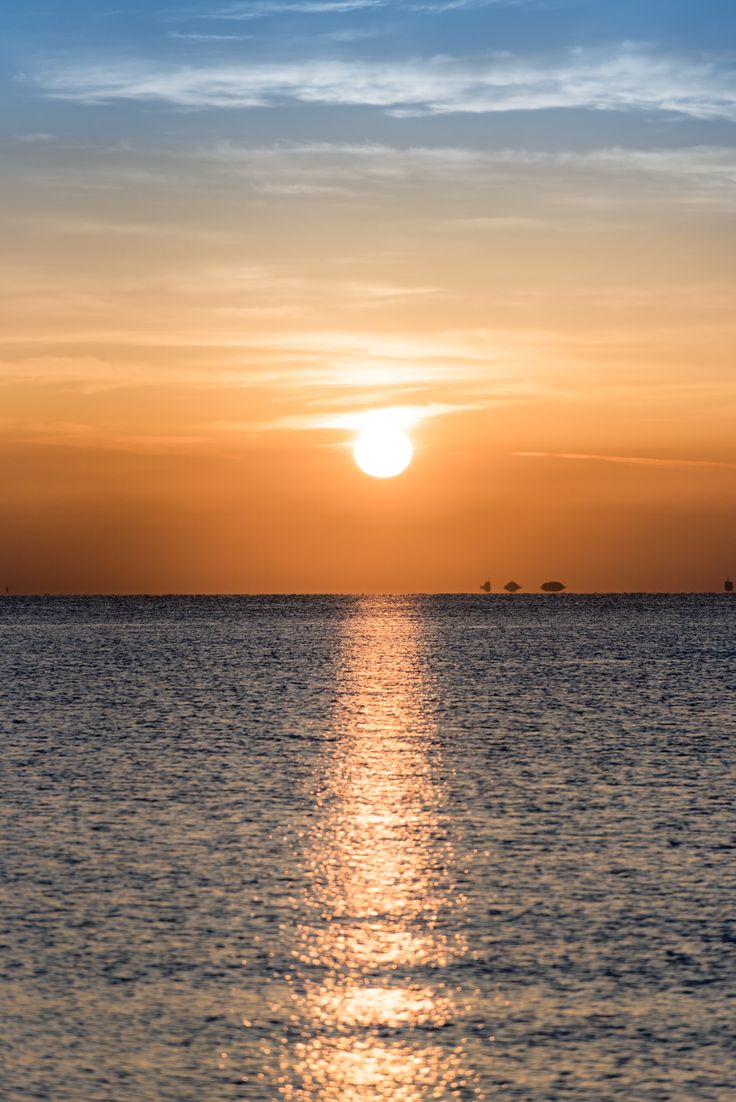 the sun is setting over the ocean with sailboats in the water and one boat on the horizon