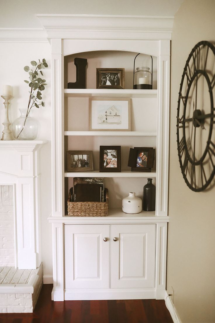 a white bookcase with pictures and other items on it in front of a fireplace