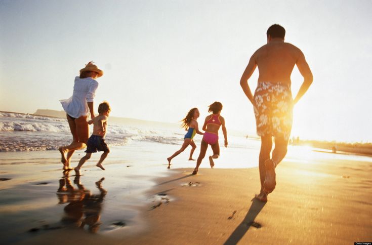 a group of people running on the beach at sunset with one person standing in the water