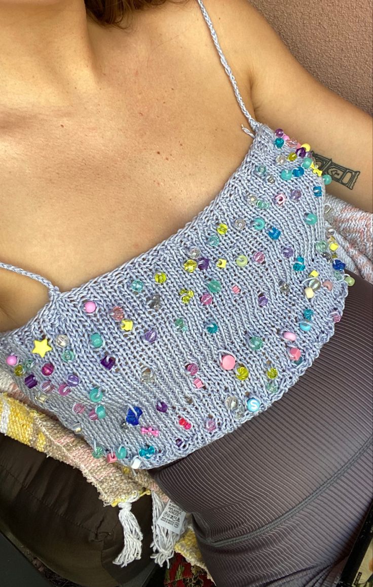 a woman sitting on a chair with her back turned to the camera, wearing a blue top with multicolored beads